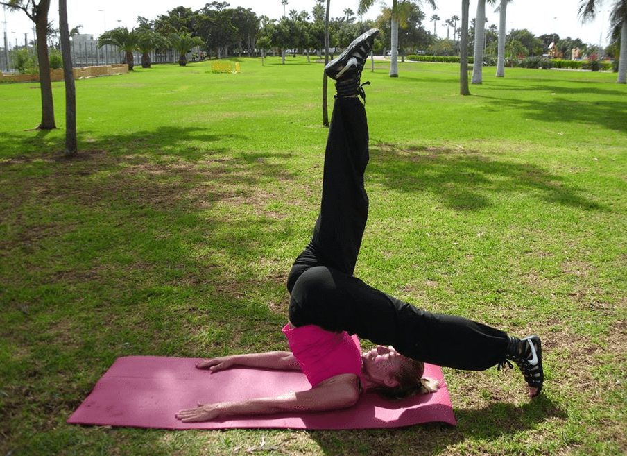 Foto de una mujer practicando una postura de yoca sobre una esterilla, en un parque